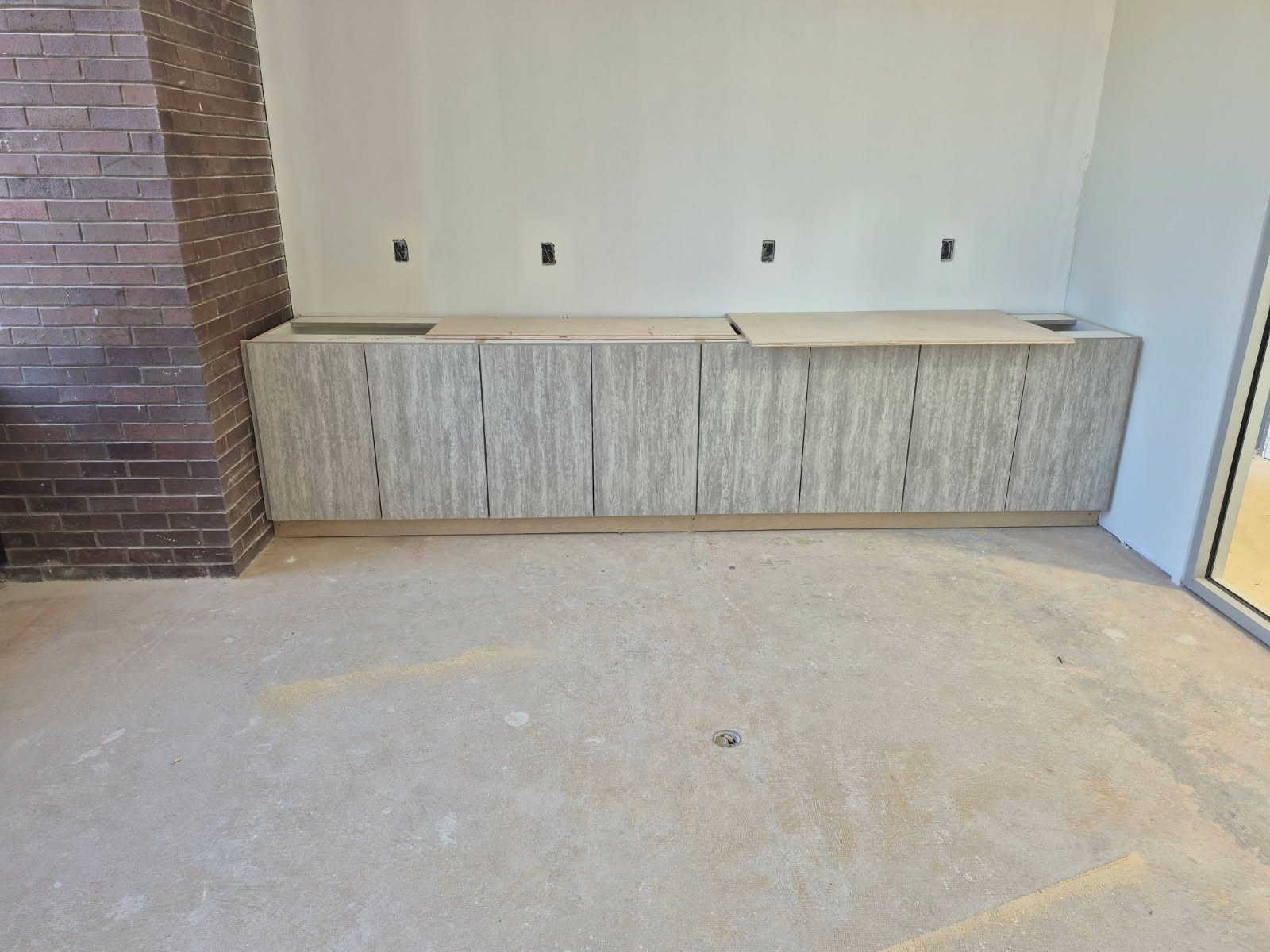 Custom laminate base cabinets installed along a brick wall in a commercial space — textured grey finish with integrated countertop cutouts