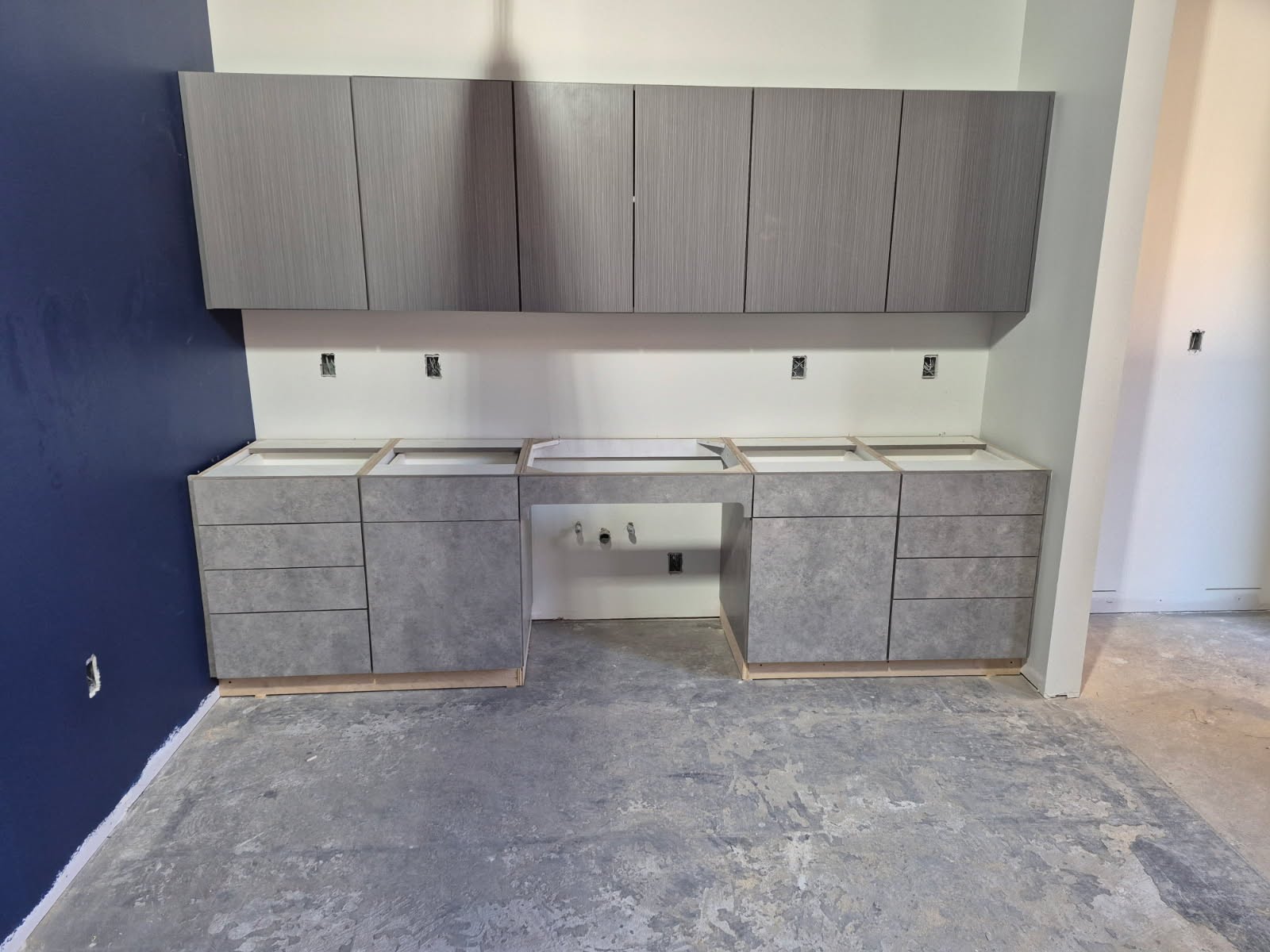 Matching upper and lower laminate cabinets installed in a commercial break room — grey textured finish with drawer banks