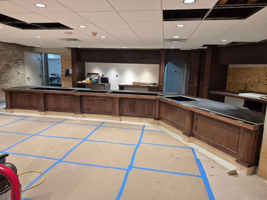 Large-scale dark wood casework and counters being installed at DeLallo's — raised panel fronts and stone countertops mid-installation